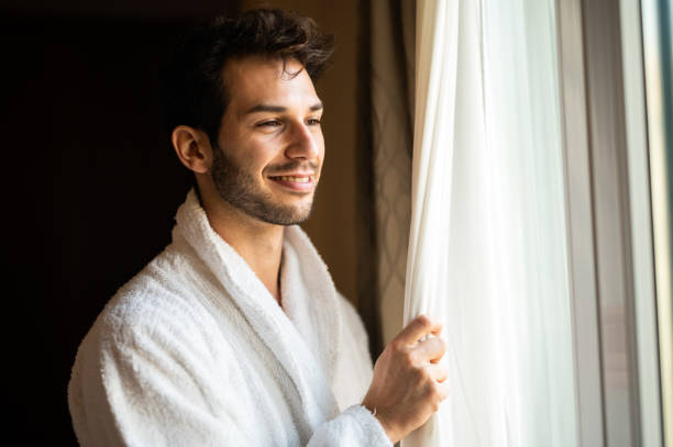 istock Young man opening curtains in hotel room 2182306970