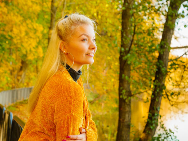 Attractive young woman wearing fashionable outfit yellow cardigan walking in autumnal park in sunny day.