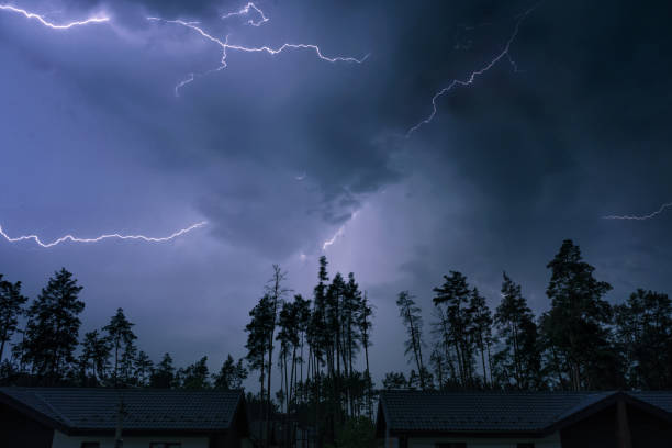 Dramatic night sky with bright lightning during a thunderstorm. Thunderstorm in the suburbs, forest and houses.