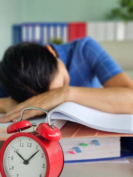 istock Tired office worker struggling to meet deadline and looking at alarm clock 2182319015
