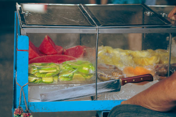 Vendor cart with assorted fruits like watermelon or tangmo, pineapple or sapparod and green mango or ma muang in plastic wrap, a popular authentic summer street food snack in Thailand