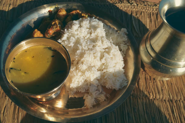 Dal bhat which is rice with lentil soup and chicken curry served on a brass plate known as chares or kaas ko thaal on a rustic straw mat showing the authentic traditional local nepali daily staple food