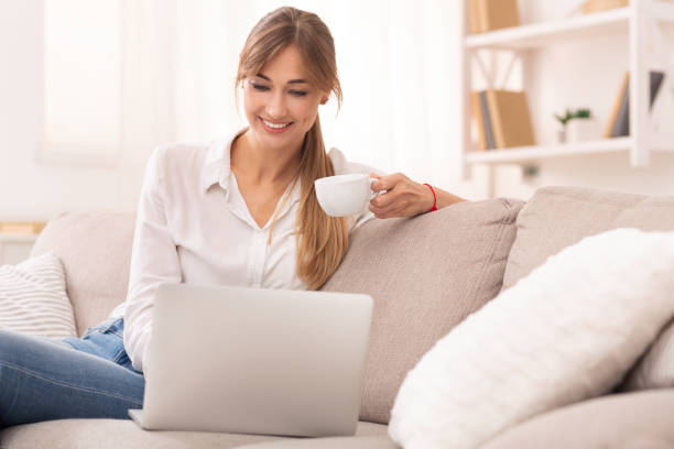 istock Cheerful Woman Using Laptop Having Coffee Sitting On Sofa 2182332848