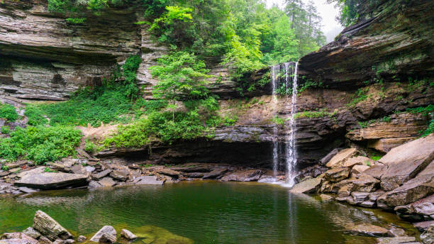 A popular swimming hole surrounded by rock cliffs and lush green foliage is below Greeter Falls in South Cumberland State Park, Tennessee.