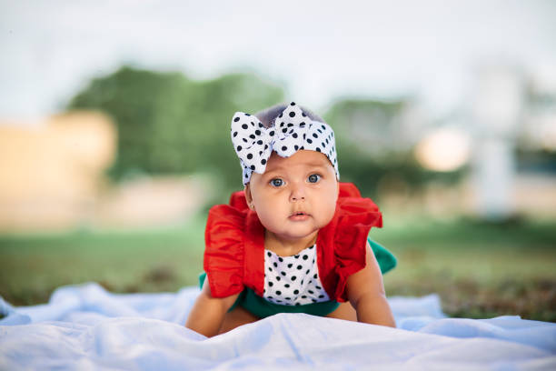 Portrait of a beautiful baby girl in a park, dressed in a beautiful polka dot dress, crrawling on a white sheet on the grass.