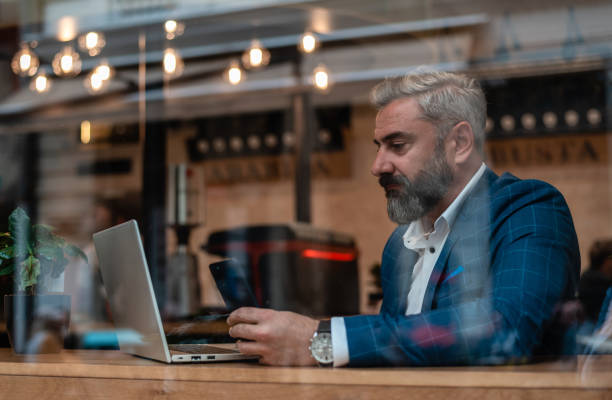 istock A handsome mature business man using his phone while working on a laptop in the office near the window. 2182351253
