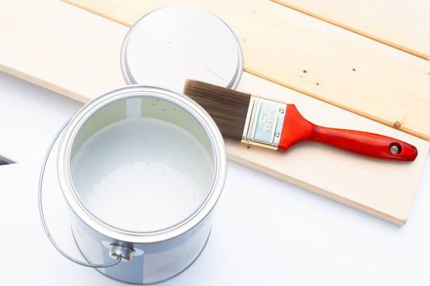 Paint can with white paint and a red paintbrush on wooden panel boards painted and unpainted.
