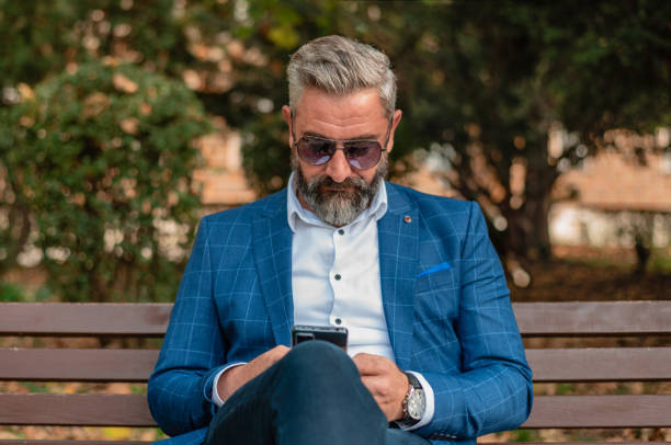 istock A handsome stylish mature business man using mobile phone app texting while sitting on the park bench. 2182352404