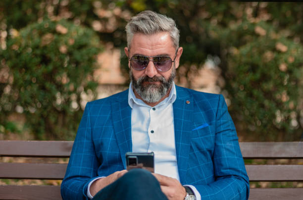 istock A handsome mature business man using mobile phone app texting while sitting on the park bench. 2182354276
