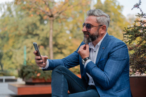 istock A handsome stylish mature business man making a video call from his mobile phone while sitting on the park bench. 2182355574