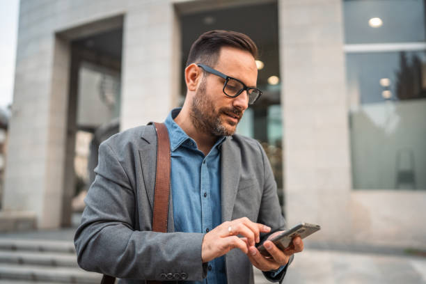 istock man businessman stand in front modern building and use mobile phone 2182360667