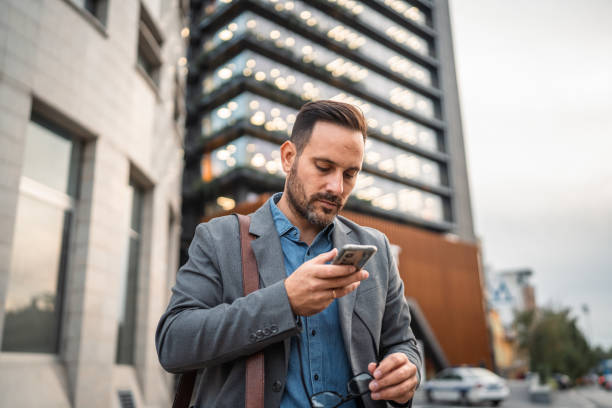 istock man businessman stand in front modern building and use mobile phone 2182360946