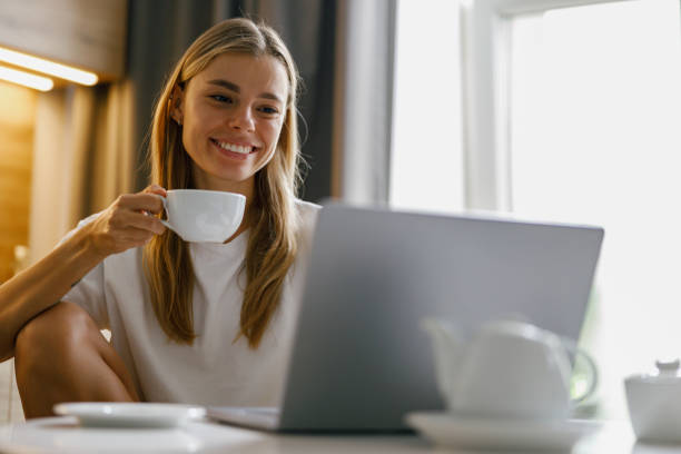istock A Young Woman is Delightfully Enjoying Her Coffee While Working on Her Laptop in a Cozy Setting 2182367530