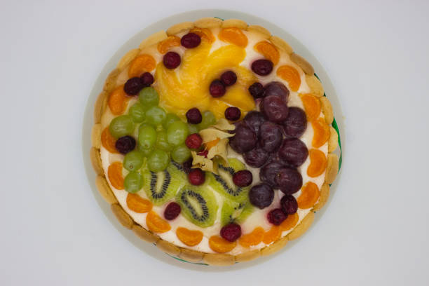 This close-up of a vibrant fruit tart highlights an array of juicy berries, grapes, kiwi, and physalis arranged on a creamy filling. The glaze adds a fresh, glossy texture that enhances the visual appeal of the dessert.