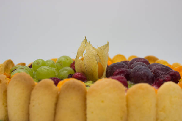 This close-up of a vibrant fruit tart highlights an array of juicy berries, grapes, kiwi, and physalis arranged on a creamy filling. The glaze adds a fresh, glossy texture that enhances the visual appeal of the dessert.