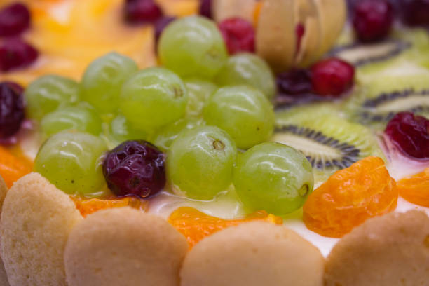 This close-up of a vibrant fruit tart highlights an array of juicy berries, grapes, kiwi, and physalis arranged on a creamy filling. The glaze adds a fresh, glossy texture that enhances the visual appeal of the dessert.