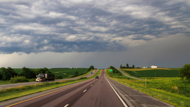 Rainfall on the horizon. Road trip through rural Iowa before storm comes. Highway surrounded by fields and cloudy sky. Driving plate