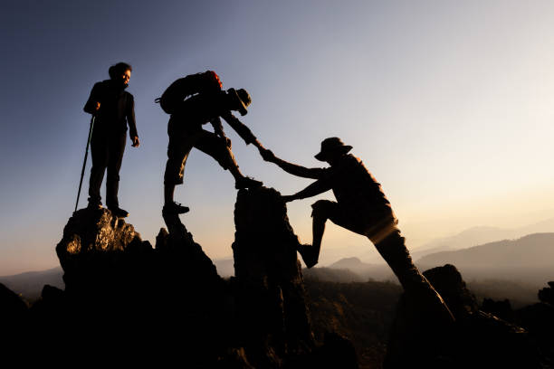 istock Silhouette of  Hikers climbing up mountain cliff. Climbing group helping each other while climbing up in sunset. Concept of help and teamwork. 2182399713