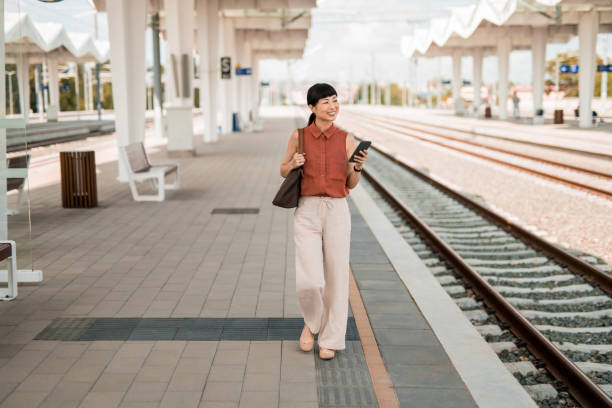 Asian woman waiting for a train on railway station and using phone.