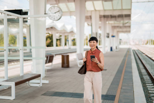 istock Asian woman waiting for a train on railway station and using phone. 2182409148
