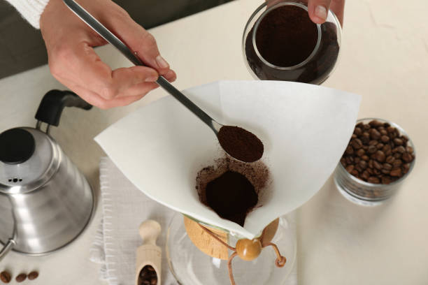 istock Making drip coffee. Woman adding ground coffee into chemex coffeemaker with paper filter at white table, closeup 2182410050