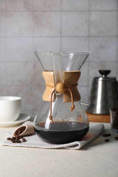 istock Glass chemex coffeemaker with tasty drip coffee and beans on white table 2182410076