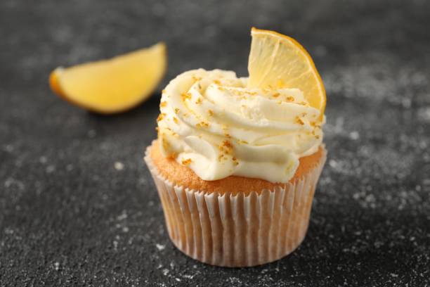 istock Tasty cupcake with cream, zest and lemon slice on black textured table, closeup 2182410941