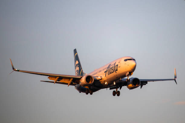 A close-up of an Alaska Airlines Boeing 737-800 as it approaches for landing at the John Wayne Airport in Santa Ana, California, bathed in golden hour sunlight. The image captures the airline’s branding and aircraft details against a clear sky, making it ideal for editorial use in aviation, travel, and airline industry publications.