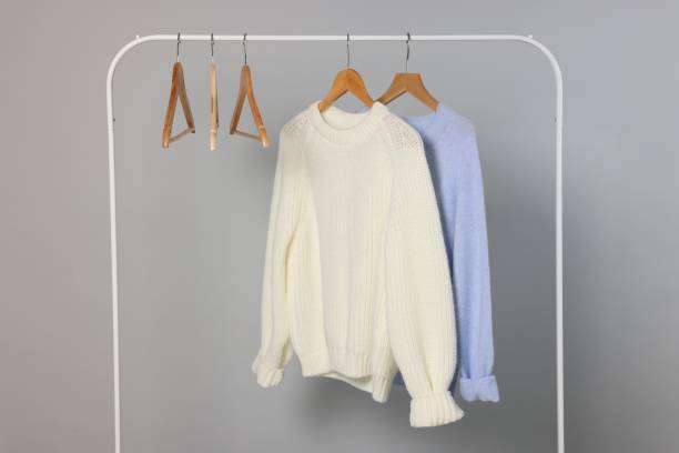 istock Rack with warm sweaters and hangers on light grey background 2182414728