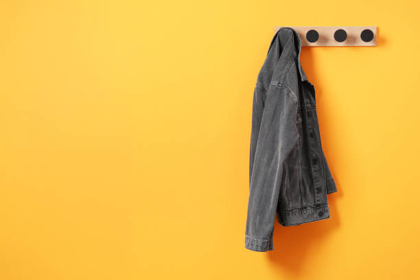 istock Rack with dark gray denim jacket on orange wall, space for text 2182414767