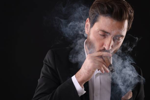istock Handsome man in elegant suit smoking cigar on black background. Space for text 2182417898