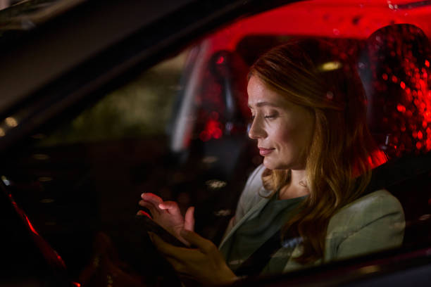 A business woman sits in a car at night, using her smartphone.