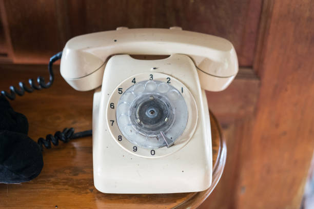 Two vintage rotary dial telephones — one beige and one red — placed side by side in a workshop or storage room. Classic devices from a bygone era with visible cords and markings.