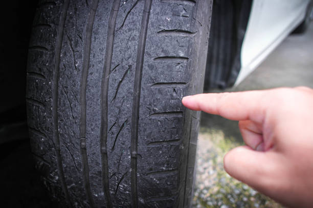 A hand pointing to worn out a car tire tread