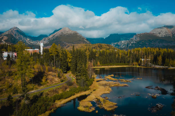 A stunning mountain lake surrounded by lush forest with majestic peaks in the background under a partly cloudy sky. The landscape captures the beauty of nature with reflections on the water and a sense of tranquility.