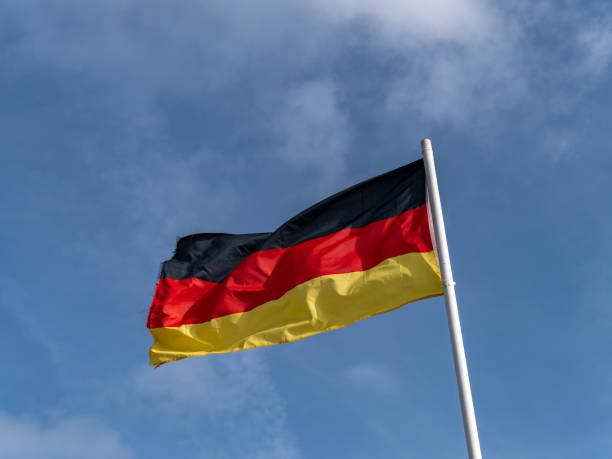istock One German flag on a flagpole against a clear blue sky. 2182455410