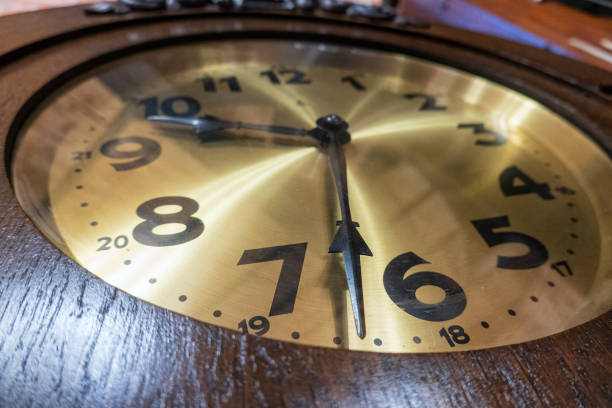 A perspective view of an antique large clock face. It has a brass plate, black hands and numbers. Close-up. Background.