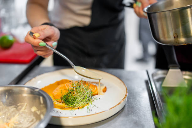 istock chef’s hands meticulously plating a gourmet dish, focusing on final sauce drizzle. elegant presentation highlights the culinary artistry and attention to detail, creating an appetizing visual appeal. 2182471042