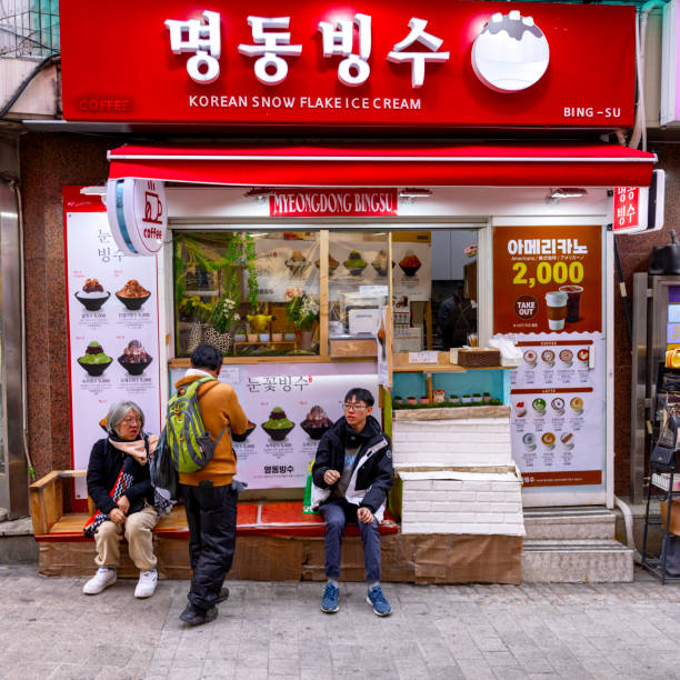 Seoul, South Korea - March 4th 2024: A Korean dessert shop specializing in bingsu, a popular shaved ice treat, with customers seated outside enjoying their orders. The storefront is adorned with bright signage and menu displays, inviting passersby to indulge in traditional Korean sweets.