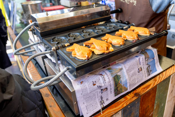 Seoul, South Korea - March 8th 2024: Fish-shaped pastries, known as bungeo-ppang, cook on a griddle at a street food stall in Seoul. These popular snacks, typically filled with sweet red bean paste, are a favorite treat among locals and tourists.