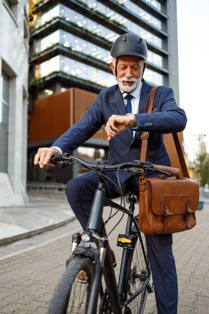 istock Senior commuter with helmet and bag checking time while traveling to work on bicycle in modern city 2182480670