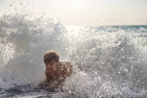 Smiling boy energetically playing at the water's edge on a bright day at the beach, happy to spend vacations on sea resort