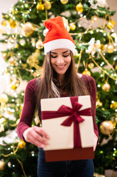 istock Young woman holding christmas gift near decorated tree 2182485509