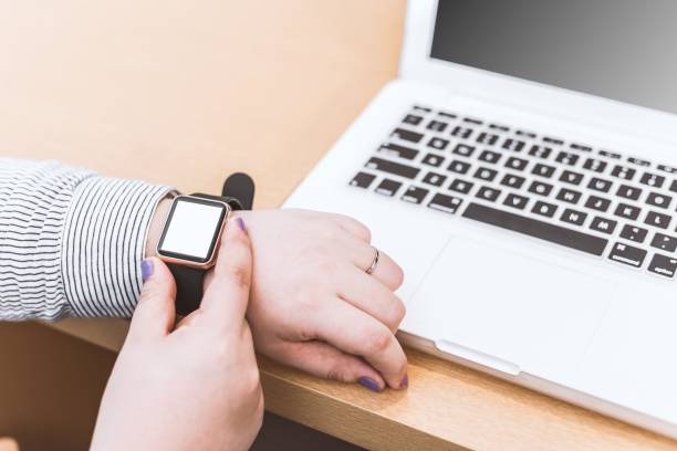 Businesswoman checking smart watch while working on laptop