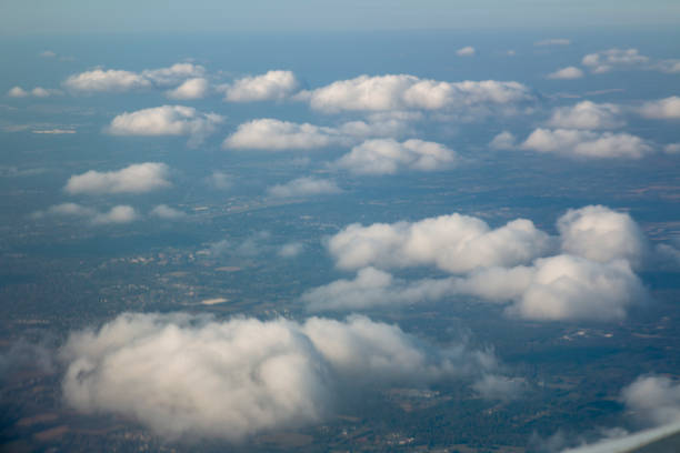 Soft, fluffy clouds float gently in a clear blue sky above a lush green landscape, showcasing a tranquil view from high above the Earth during the day.