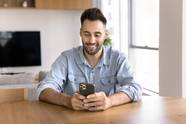 istock Positive Hispanic man typing on mobile phone at home workplace 2182498044