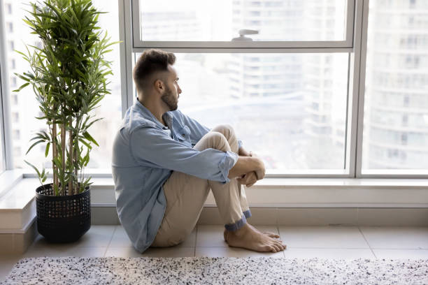 istock Frustrated lonely Latin man sitting at large window on floor 2182498559