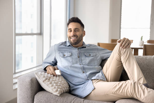 istock Happy attractive Hispanic guy watching TV, resting on home couch 2182498759