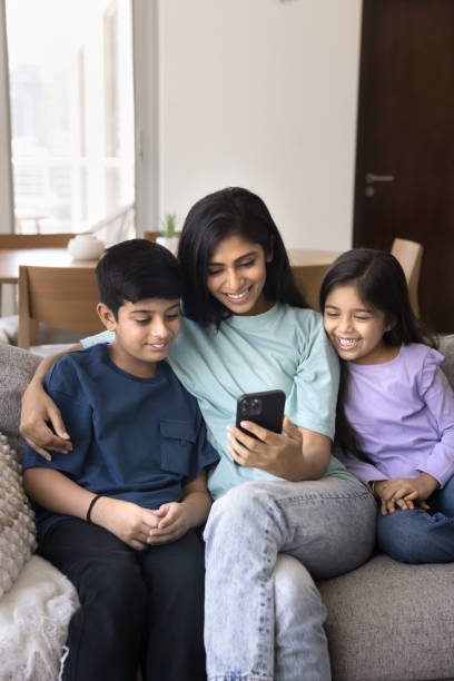 istock Positive young Indian mother using smartphone, hugging son and daughter 2182503999