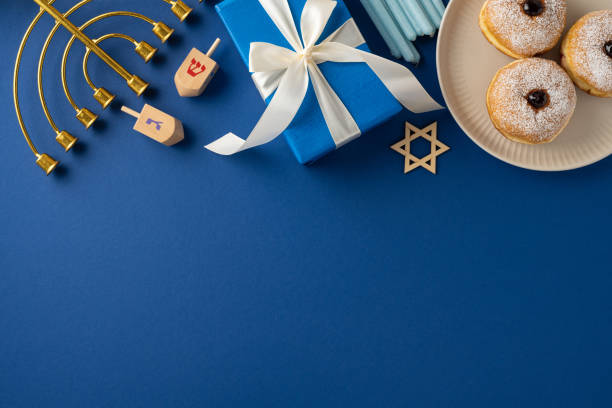 istock A Hanukkah celebration setup featuring a menorah, dreidels, gifts, and traditional donuts on a blue background. The elements evoke the festive and joyful spirit of the Hanukkah holiday 2182505513